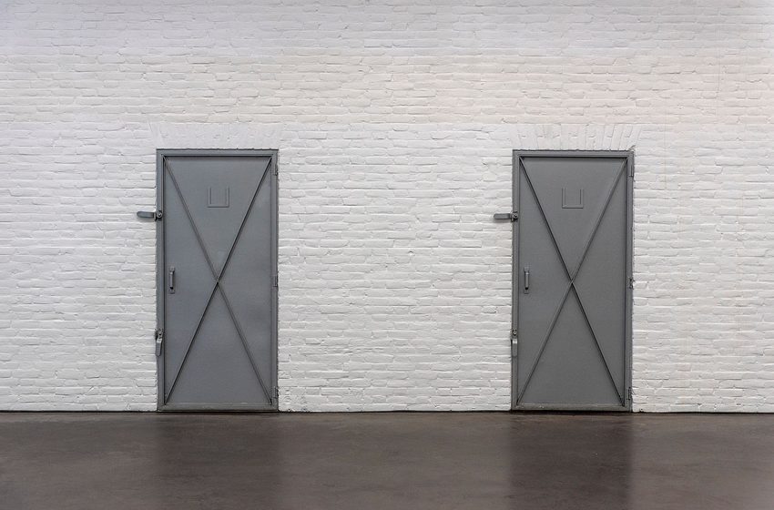 Two gray steel doors on a white brick wall