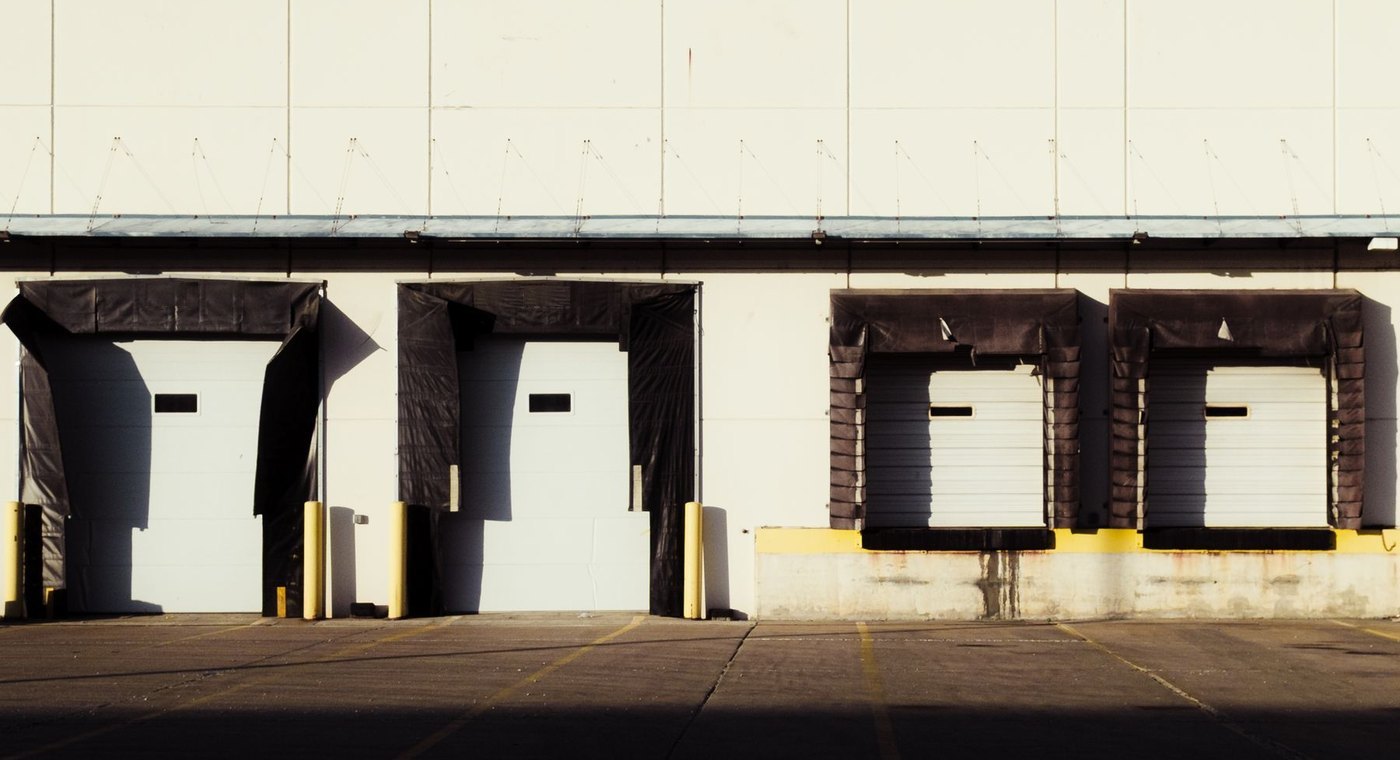 Four white overhead loading dock doors with dock shelters on a warehouse wall
